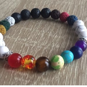 Op de afbeelding: Een armband met zwarte, witte, rode, oranje, bruine, groene, blauwe en paarse kralen. De kralen zijn gerangschikt in een regenboogpatroon.