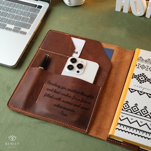 Może przedstawiać: Brązowy sk&oacute;rzany notes z telefonem i długopisem w środku. Notes zawiera spersonalizowany napis: "Sending you positive thoughts and best wishes for a future filled with success and great achievements. -Tom".