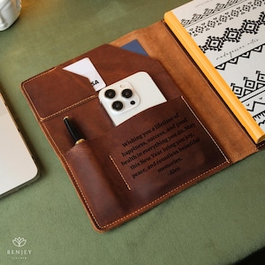 May include: A brown leather journal with a personalized message wishing someone a lifetime of happiness, success, and good health. The journal has a pocket for a phone and a pen.