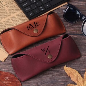 Pode incluir: Duas capas de &oacute;culos de couro, castanho e bord&ocirc;, cada uma com um monograma personalizado. A capa castanha tem as iniciais "HME", e a bord&ocirc; "W/T". Ambas as capas t&ecirc;m um fecho de press&atilde;o.
