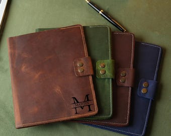 Könnte beinhalten: Vier ledergebundene Notizbücher in Braun, Grün, Braun und Blau. Das braune Notizbuch trägt den Namen "Martin" und das Initial "M" ist auf der Vorderseite eingraviert.
