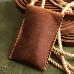 May include: A brown leather pouch with white stitching. The pouch is made from soft, supple leather and has a rustic, vintage look.