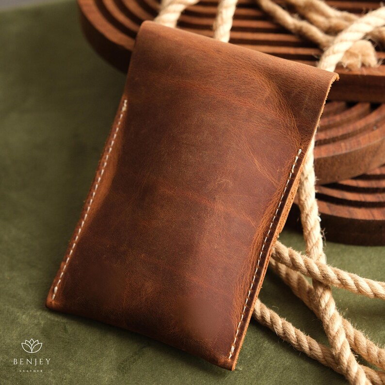 May include: A brown leather pouch with white stitching. The pouch is made from soft, supple leather and has a rustic, vintage look.
