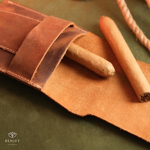 May include: A brown leather cigar case with two cigars inside. The case has a flap that closes with a snap.