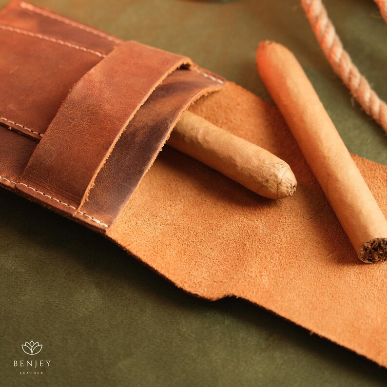 May include: A brown leather cigar case with two cigars inside. The case has a flap that closes with a snap.