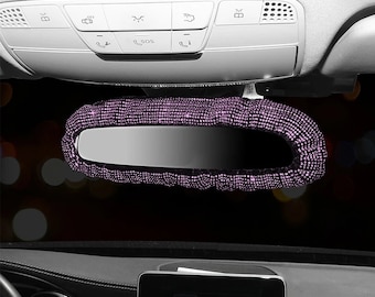 May include: A car rearview mirror with a purple rhinestone cover. The cover is made of small, sparkling rhinestones that completely encase the mirror. The mirror is mounted on the car's ceiling, with various control buttons visible above.