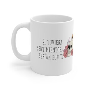 May include: White ceramic mug with a black skull and floral design. The text on the mug reads "Si tuviera sentimientos, serían por ti."
