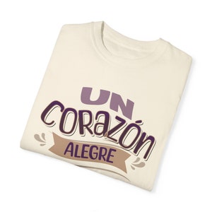 May include: A white t-shirt with the text "UN CORAZÓN ALEGRE" in purple and brown lettering.