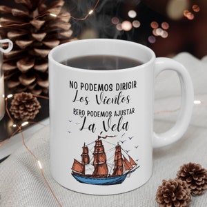 May include: White ceramic coffee mug with a black handle. The mug features a black and white illustration of a sailing ship with the text "No podemos dirigir los vientos pero podemos ajustar la vela".
