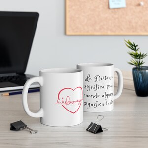 May include: Two white ceramic mugs with black text and a red heart. The text on the mug reads "La Distancia Significa poco, cuando alguien Significa tanto".