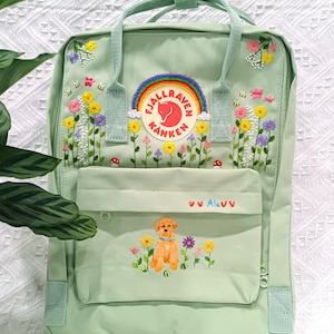May include: A light green backpack with embroidered flowers, bees, and a rainbow logo. The front pocket features a dog illustration and the name "Alevv". The backpack has a top handle and adjustable straps.