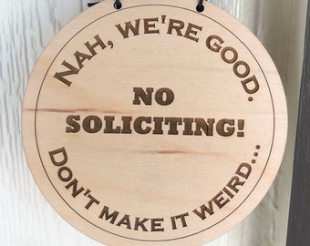 Könnte beinhalten: Ein rundes Schild aus Holz mit dem Text "Nah, we're good. No soliciting! Don't make it weird..." Das Schild hängt an einer Tür neben einer schwarzen Türklingelkamera.