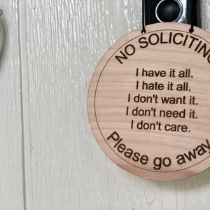 K&ouml;nnte beinhalten: Ein rundes Schild aus Holz mit dem Text "NO SOLICITING" in einem Kreis um den Rand. Das Schild hat auch den Text "I have it all. I hate it all. I don't want it. I don't need it. I don't care. Please go away."