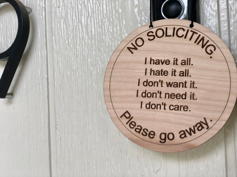 K&ouml;nnte beinhalten: Ein rundes Schild aus Holz mit dem Text "NO SOLICITING" in einem Kreis um den Rand. Das Schild hat auch den Text "I have it all. I hate it all. I don't want it. I don't need it. I don't care. Please go away."