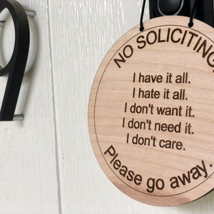 K&ouml;nnte beinhalten: Ein rundes Schild aus Holz mit dem Text "NO SOLICITING" in einem Kreis um den Rand. Das Schild enth&auml;lt auch den Text "I have it all. I hate it all. I don't want it. I don't need it. I don't care. Please go away."