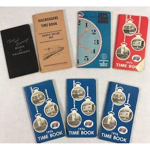 May include: A collection of vintage railroad time books. The books are blue, red, and black with a variety of designs. The books feature the text "Time Book" and the year 1974, 1975, and 1976.