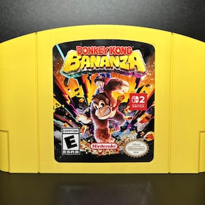 Könnte beinhalten: Gelbe Nintendo 64-Spielkassette mit dem Spiel "Donkey Kong Bananza". Das Etikett des Spiels zeigt Donkey Kong und andere Charaktere in einer farbenfrohen Action-Szene. Die Kassette hat die ESRB-Bewertung "Everyone".