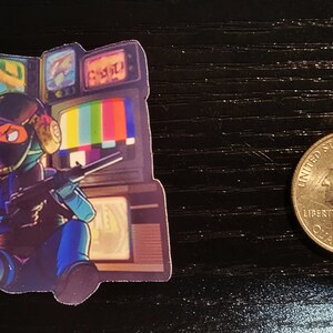 May include: A sticker featuring a cartoon character wearing a black helmet and holding a gun. The character is sitting in front of a wall of old televisions with static and other images on the screens.