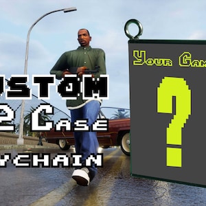 May include: A custom PlayStation 2 game case keychain with a question mark in pixel art. The keychain is gray with a green border and a yellow question mark. The text "Your Game" is printed in pixel art on the keychain.