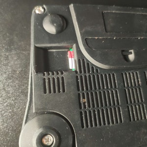 Op de afbeelding: Close-up van de achterkant van een zwarte Nintendo 64 console. De console heeft een slot voor een geheugenkaart, een ventilatieopening en een schroef.