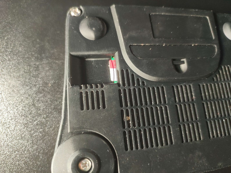 Op de afbeelding: Close-up van de achterkant van een zwarte Nintendo 64 console. De console heeft een slot voor een geheugenkaart, een ventilatieopening en een schroef.