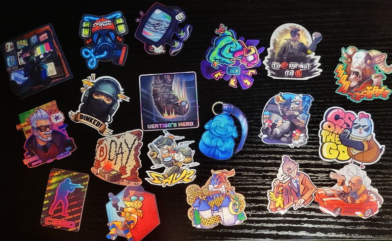 May include: A collection of colorful stickers featuring various designs related to the video game Counter-Strike: Global Offensive. The stickers include characters, weapons, and logos from the game. Some of the stickers have text, such as "Dinked!" and "CS on the GO".