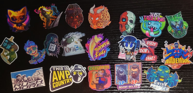 May include: A collection of 20 colorful stickers featuring various designs, including a skull with flames, a cartoon character with a peace sign, a dragon, a gamer character, and a skull with a gas mask. The stickers are on a black surface.