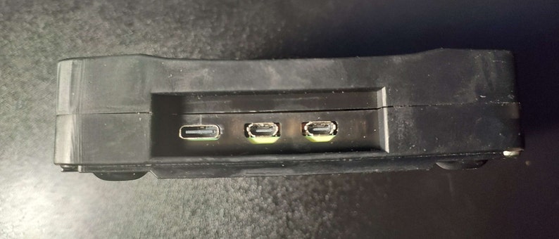 Op de afbeelding: Een zwart rechthoekig apparaat met drie USB-poorten aan de zijkant.