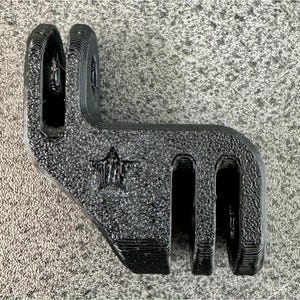 Puede incluir: Soporte de cámara de plástico negro con un logotipo en forma de estrella. El soporte tiene tres ranuras para sujetar una cámara.