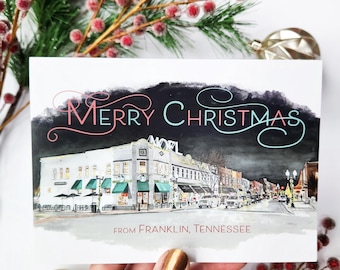 May include: A Christmas card with the words "Merry Christmas" in pink and blue script over a watercolor illustration of a street scene. The card reads "From Franklin, Tennessee."