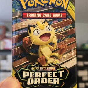 May include: A Pokémon Trading Card Game booster pack featuring Meowth. The pack has the Pokémon logo and the text "Trading Card Game". The bottom of the pack reads "Mega Evolution Perfect Order" and "10 Additional Game Cards".