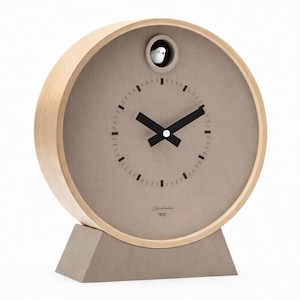 May include: A modern, round cuckoo clock with a light wood frame and a taupe face. The clock features black hands, a small bird, and a gray base. The clock face has a minimalist design with small black markers.