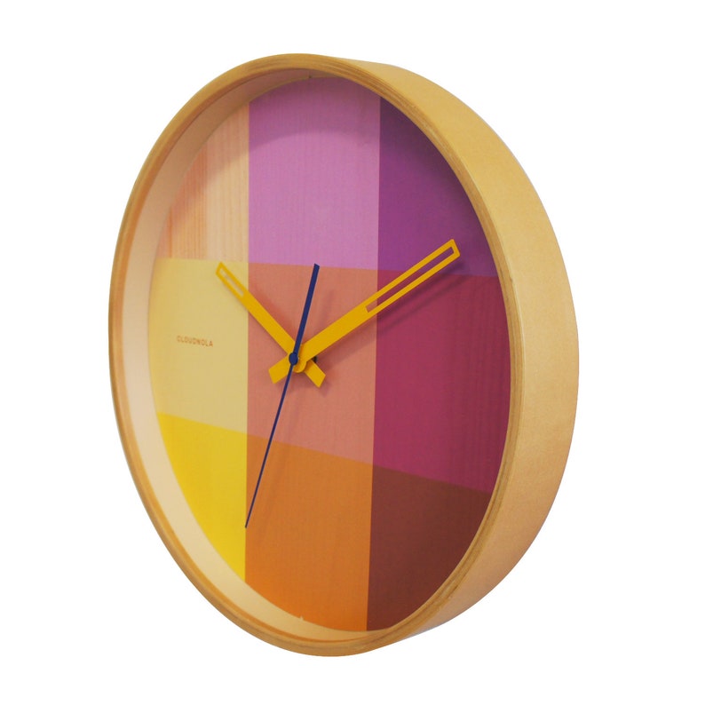 This trendy 30 cm wooden wall clock has a vibrant printed clock face with the pattern of colorful squares in a mix of yellow & magenta. The silent clock is finished with a oker yellow hour and minute hand and a smooth moving dark blue second hand.