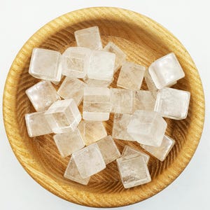 May include: A wooden bowl filled with clear quartz crystal cubes. The crystals are smooth and translucent, with a slight sparkle.