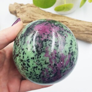 May include: Green, pink and black gemstone sphere. The sphere is polished and has a smooth surface.