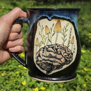 May include: A set of three ceramic mugs with a speckled, matte finish. The mugs are in shades of cream, light gray, and dark gray. Each mug has a simple, minimalist design and a rounded handle.