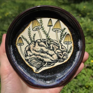 May include: A white ceramic mug with a black handle and the text "But First, Coffee" in a bold, black font. The mug is set against a blurred background, suggesting a cozy setting.