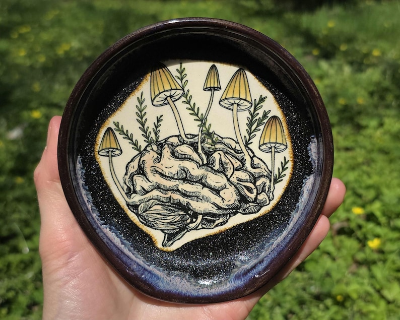 May include: A white ceramic mug with a black handle and the text "But First, Coffee" in a bold, black font. The mug is set against a blurred background, suggesting a cozy setting.