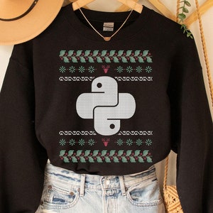 Peut inclure: Sweat-shirt noir avec un logo Python blanc sur un motif de pull de Noël vert et rouge. Le sweat-shirt est porté sur un short en jean bleu clair.