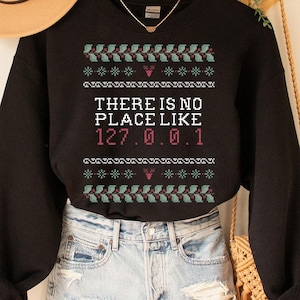May include: Black sweatshirt with a green and white snowflake pattern and the text "THERE IS NO PLACE LIKE 127.0.0.1" in pink.