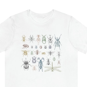 May include: White t-shirt featuring a colourful illustration of various insects, including beetles, butterflies, and dragonflies.