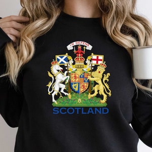 May include: Black sweatshirt with a gold and white royal coat of arms featuring a unicorn and lion. The text "IN DEFENS" and "SCOTLAND" are printed on the sweatshirt.