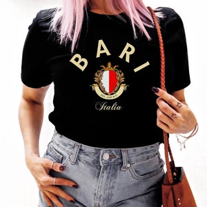 以下が含まれることがあります： 前面に金の紋章と「BARI Italia」の文字がプリントされた黒いTシャツです。