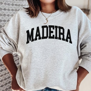 May include: A gray sweatshirt with the word "MADEIRA" printed in black across the front. The sweatshirt has a crew neck and long sleeves.