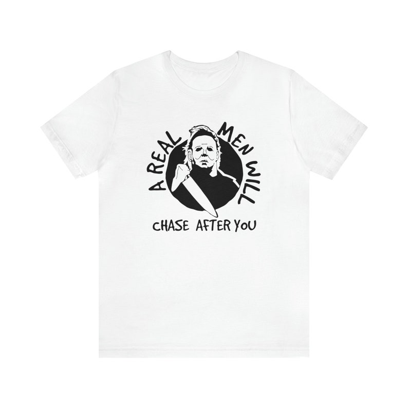 May include: White t-shirt featuring a black and white graphic of a man holding a knife. The graphic is in a circle with the text "A Real Men Will Chase After You".