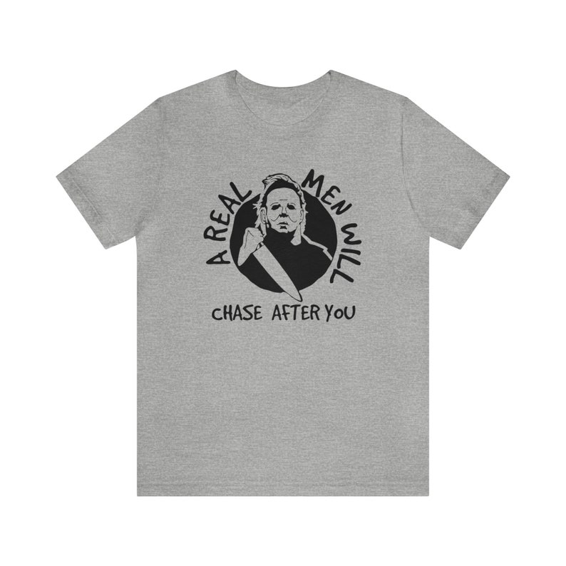 May include: A grey t-shirt with a black graphic of a man holding a knife. The graphic is in a circle with the text "A Real Men Will Chase After You".