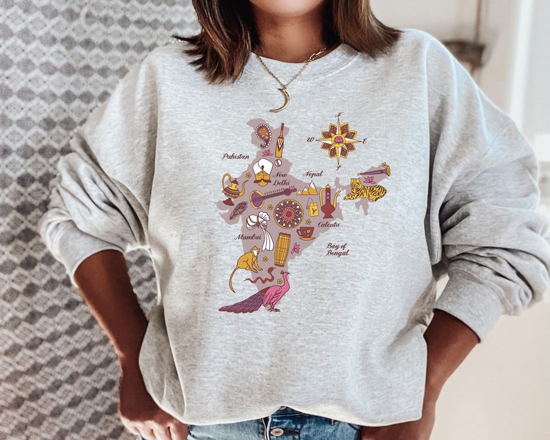 May include: A gray sweatshirt with a graphic print of a map of India. The map is filled with illustrations of various cultural icons, including a peacock, a tiger, a monkey, a teacup, and a musical instrument. The text "Pakistan", "New Delhi", "Nepal", "Calcutta", and "Bay of Bengal" is printed on the map.