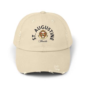 May include: A beige distressed baseball cap with a black embroidered logo that says "ST. AUGUSTINE, EST. 1565, Florida".