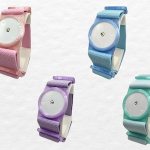 May include: Four circular glucose monitor covers with adjustable fabric bands in pastel pink, light blue, lavender, and mint green. Each cover features a white center disc with a small metallic detail, held by a matching colored plastic frame.