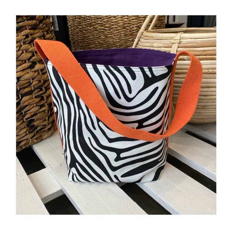 Puede incluir: Una bolsa de mano de lona con estampado de cebra en blanco y negro, con una correa naranja y un forro morado.